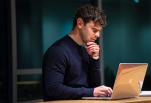 mężczyzna w czarnej koszuli z długim rękawem siedzi przed macbookiem